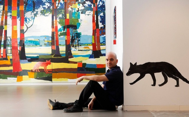 Foto de Manuel Pérez pintor y artista. posando junto alguna de sus obras.